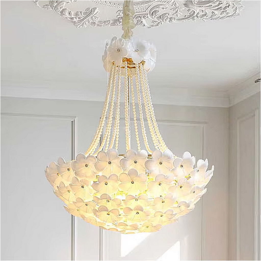 Elegant chandelier glowing softly in a white minimalist living room, adorned with handcrafted white flower motifs and cascading beaded strands.