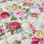 Floral quilt with pink, red, and yellow roses on a ivory bed spread in Cottagecore bedroom