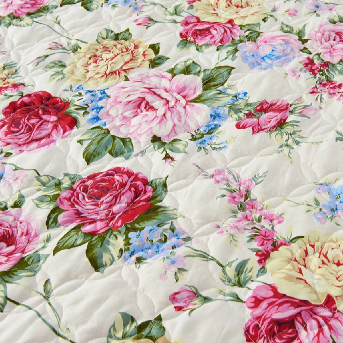 Floral quilt with pink, red, and yellow roses on a ivory bed spread in Cottagecore bedroom