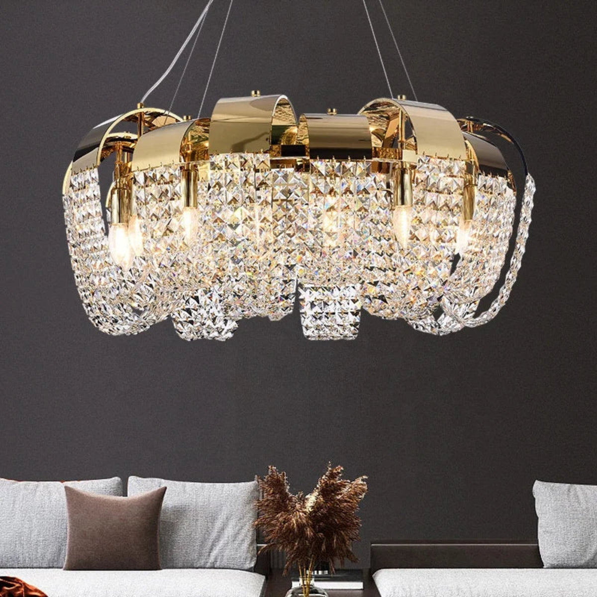 Gold and crystal chandelier hanging above a gray sofa with decorative pillows and a plant.