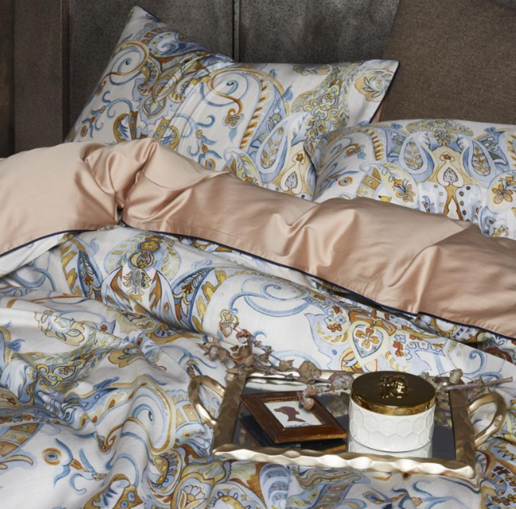 Side angle showing soft Egyptian cotton pillowcases and folded duvet with printed motif, resting over a warm beige flat sheet.