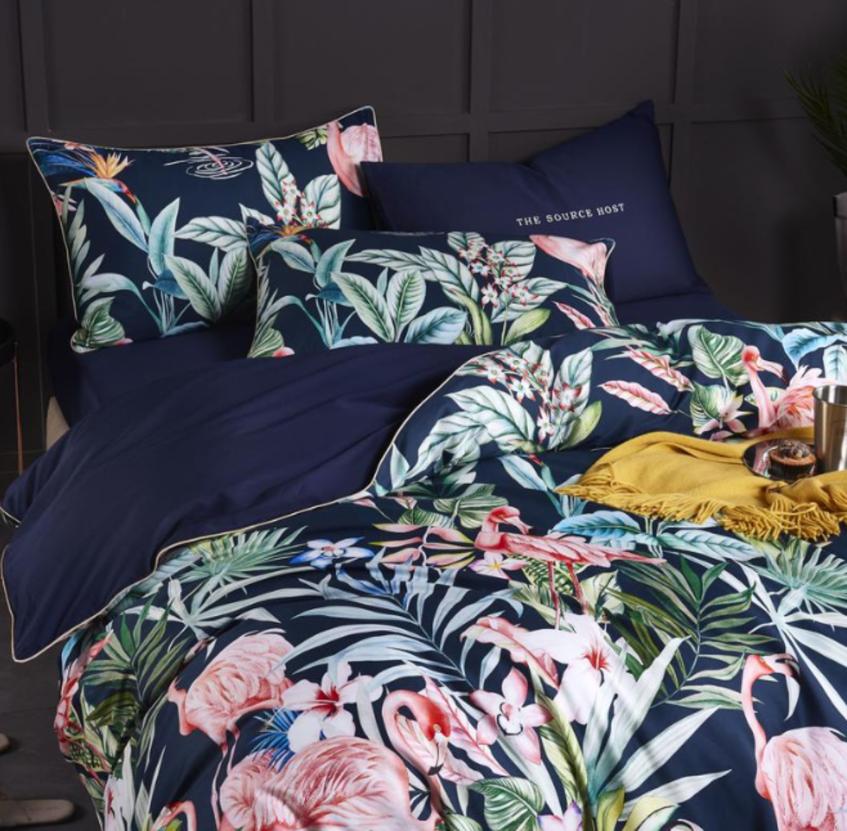 Close-up of 4-piece bedding set with navy flat sheet, matching tropical print pillows, and silky flamingo-patterned duvet.
