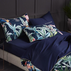 Folded duvet revealing dark navy interior, with two tropical pillows atop navy flat sheet — emphasizing bold color contrast and botanical energy.