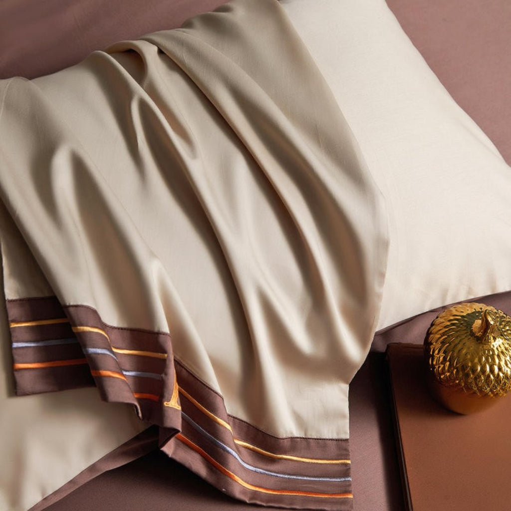 Detail of satin-finish beige duvet edge with H-stitched brown border – soft minimalist bedding texture