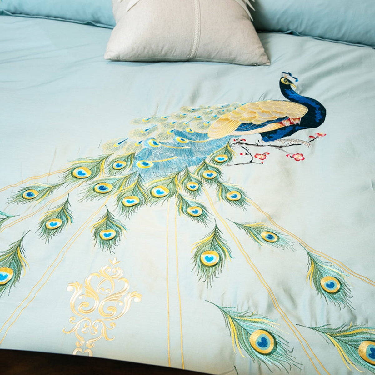 Detailed embroidery of peacock feathers in green, blue, and gold thread on luxury Egyptian cotton duvet.