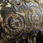 Close-up of gold embroidered motif on grey pillowcase, showcasing intricate baroque pattern and stitching quality.