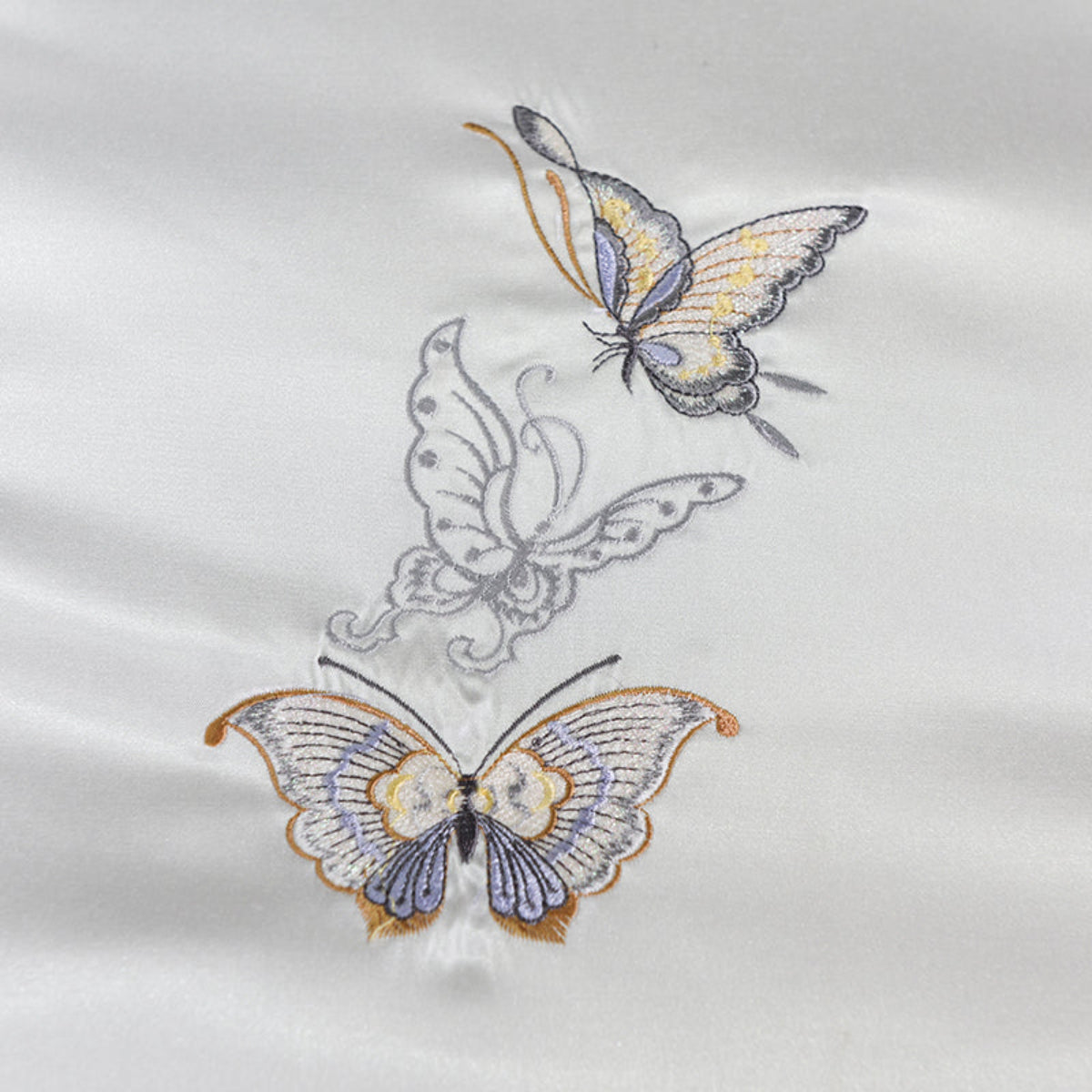 Close-up of the embroidered butterfly design on the duvet cover, showcasing tribute silk craftsmanship and fine detail.