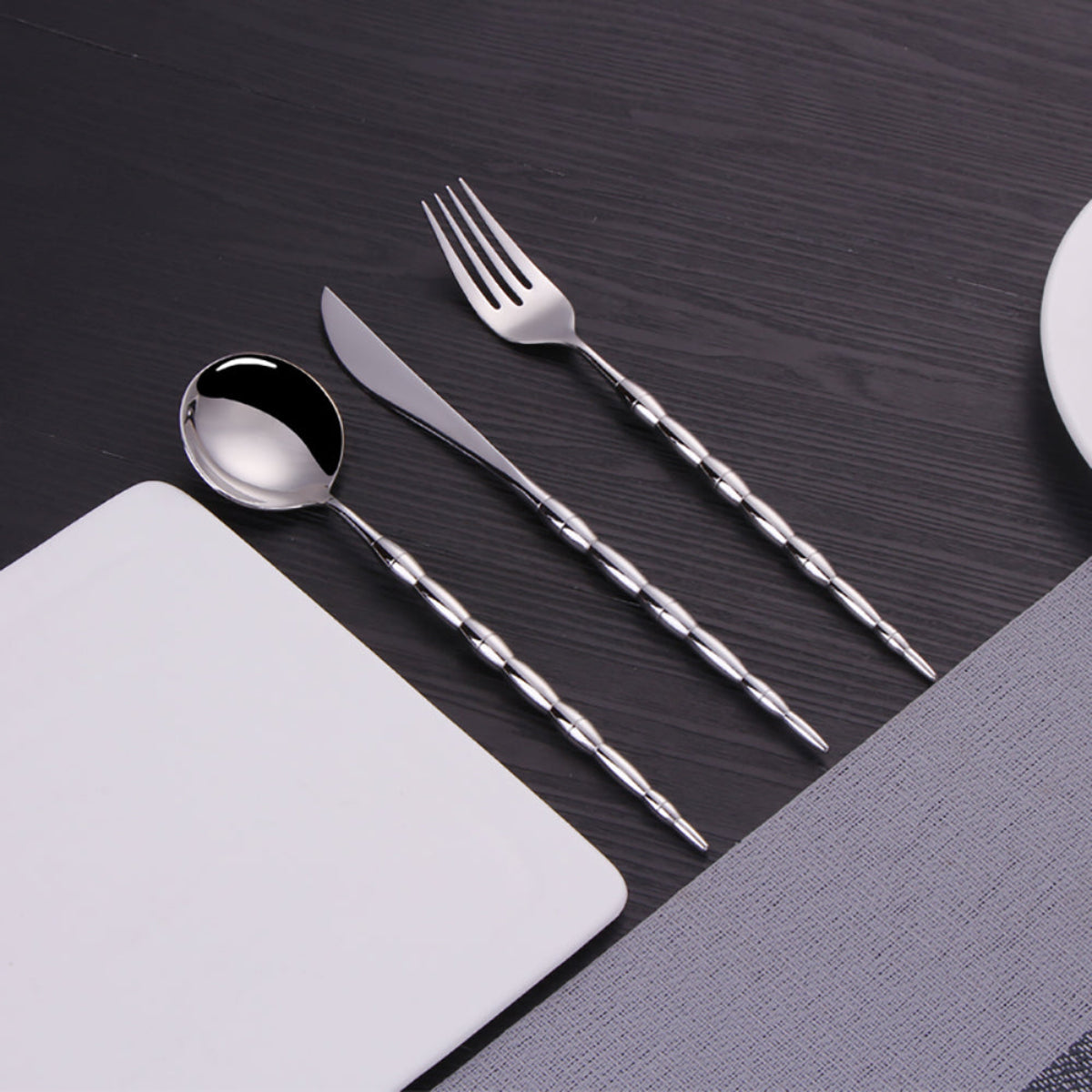 Elegant silver flatware set with sculptural beaded stems and minimalist heads, displayed on white marble surface with dining accessories