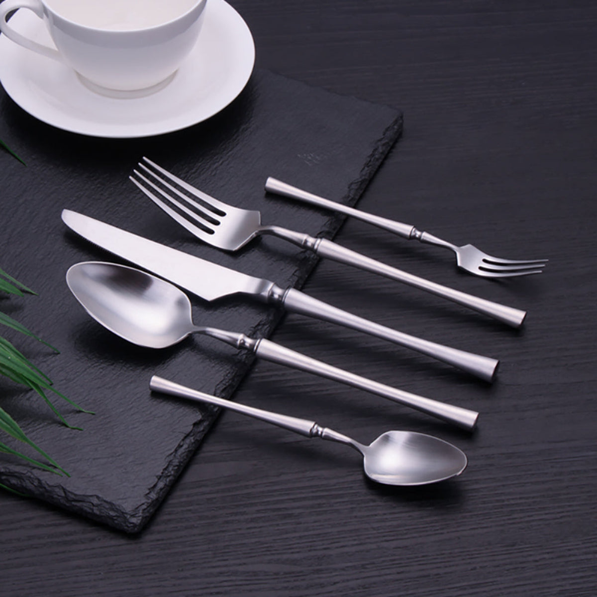 Minimalist silver flatware set styled on textured black surface — modern dining table cutlery for luxury entertaining, LINKORI Lilla Silver top view.